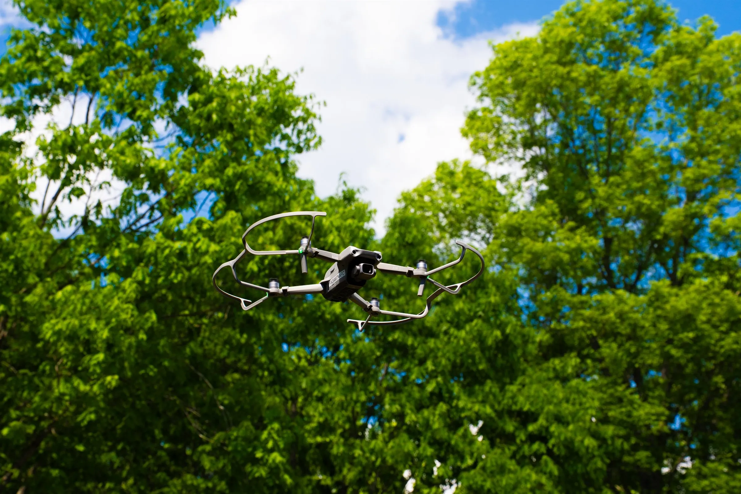 DJI Air 2S drone hovering in front of tall green trees