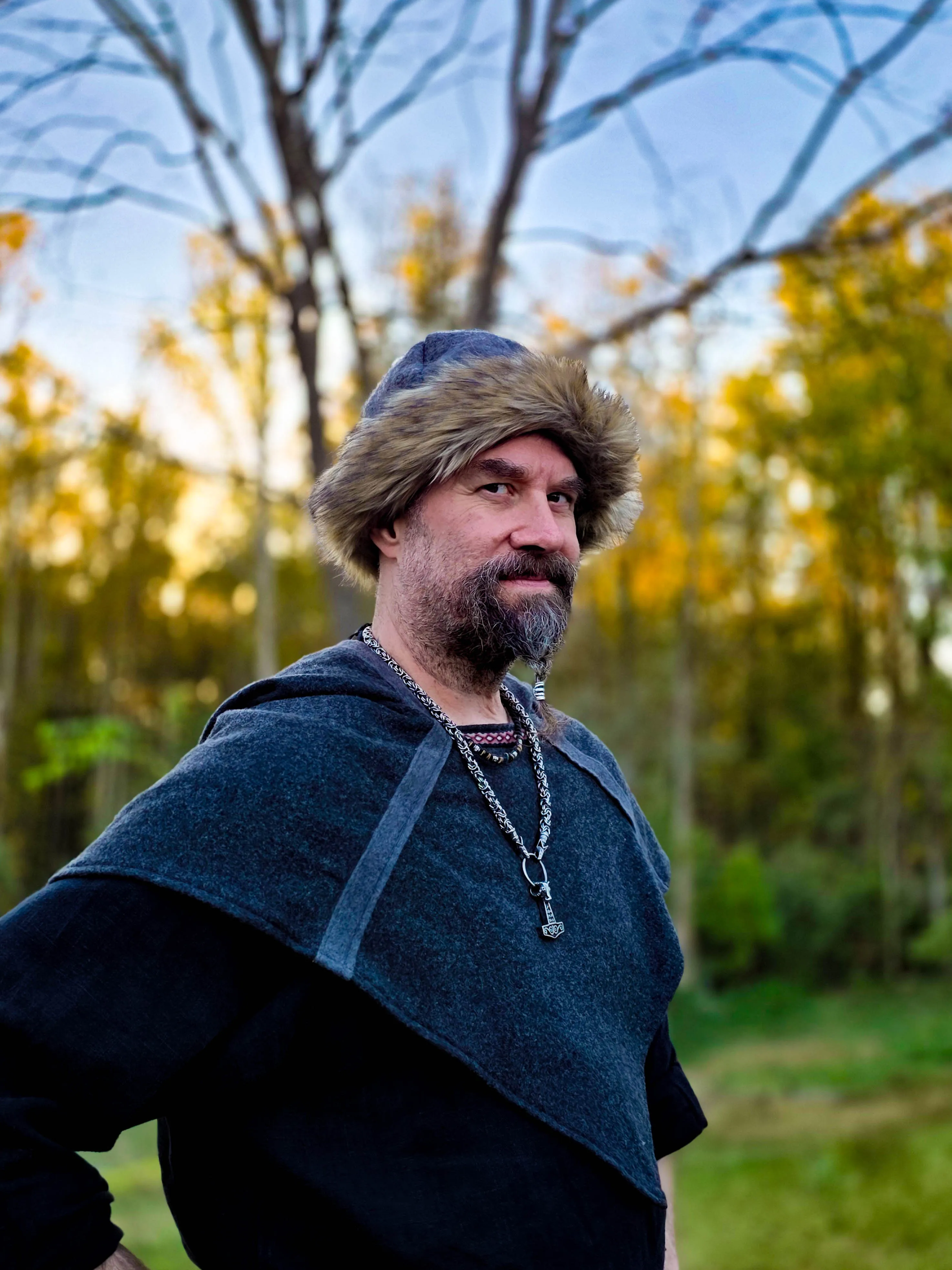 Smedis in a fur hat and wool hood, standing among autumn trees